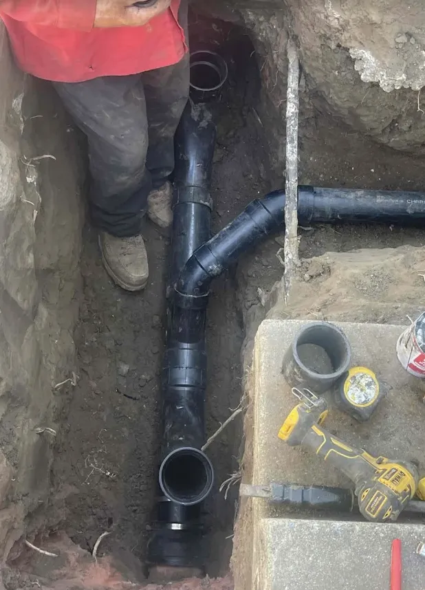 Sewer line replacement: new ABS pipe, fittings, and a coupling set in an open trench